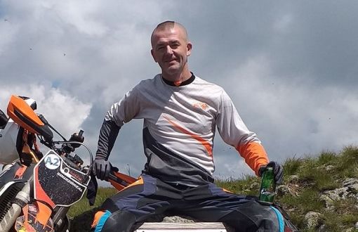 Prof. A. Niewiadomski w motocyklowym stroju sportowym siedzi na skale. Obok ubłocony motor.