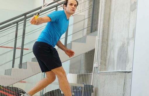 Prof. Tomasz Czyszanowski w niebieskiej koszulce i krótkich spodenkach odbija piłkę podczas gry w squasha