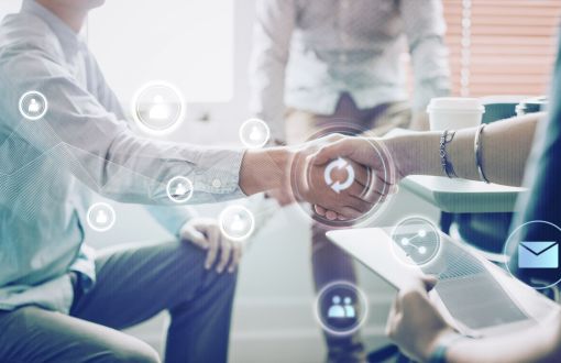 Zdjęcie poglądowe: uścisk dłoni dwójki ludzi. Na pierwszym planie białe i przeźroczyste ikonki symbolizujące komunikację.