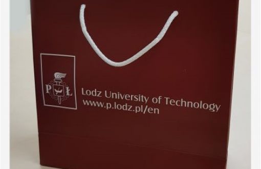 Maroon, square paper bag with white ear and the inscription Lodz University of Technology in Polish and English.