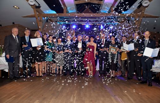 Elegancko ubranych kilkunastu pracowników Wydział z pamiątkowymi dyplomami. W tle błyszczące konfetti.