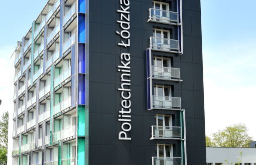 8 piętrowy budynek akademika uczelni. Ściana frontowa czarna z pionowym napisem Politechnika Łódzka. Ścianę boczną tworzą przeszklone balkony.