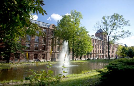 Kampus B Politechniki Łódzkiej: staw, zielony trawnik i kilka drzew, w tle ceglany Budynek Trzech Wydziałów.
