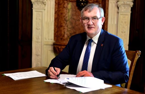 Rektor PŁ, prof. Krzysztof Jóźwik w swoim gabinecie siedzi przy drewnianym biurku i podpisuje dokumenty.