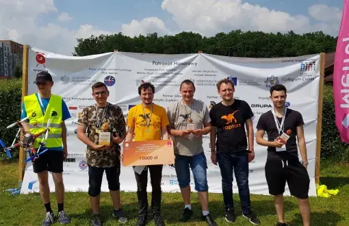 Sześciu członków zespołu Raptorsi na tle ścianki reklamowej zawodów. Jeden z nich trzyma dron, drugi symboliczny czek.