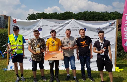 Sześciu członków zespołu Raptorsi na tle ścianki reklamowej zawodów. Jeden z nich trzyma dron, drugi symboliczny czek.