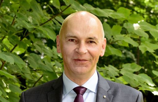 dr hab. inż. Witold Pawłowski, prof. PŁ w szarym garniturze, białej koszuli i bordowym krawacie na tle zieleni.