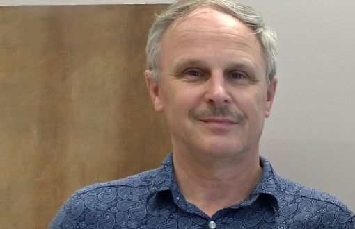 Adam Rylski w niebieskiej koszuli z krótkim rękawek trzyma pamiątkową, srebrną statuetkę oraz dyplom.