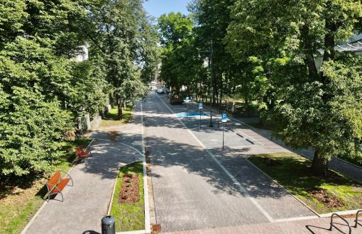 Zdjęcie z góry woonerfu na ul. Stefanowskiego. Po bokach wysokie, zielone drzewa, w środku, po lewej stronie chodni i ławki, po prawej ulica z szarej kostki.