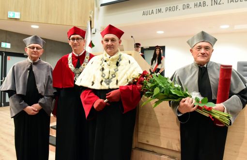 W reprezentacyjnej auli od prawej strony stoją w togach: prof. Klaus Müllen, który trzyma bukiet róż, prof. Krzysztof Jóźwik, prof. Łukasz Albrecht i prof. Jacek Ulański.