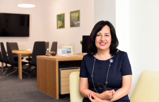 Prof. Iwona Szynkowska-Jóźwik w granatowej sukience na tle biura: w tle biurko, stół do pracy zbiorowej.