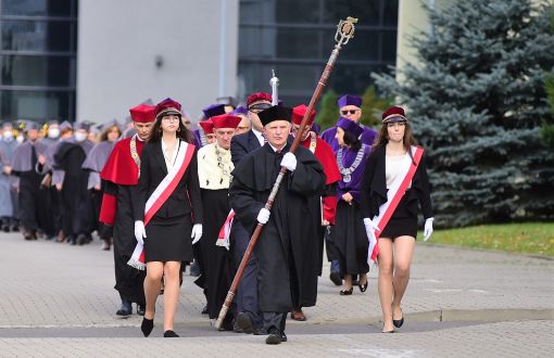 Społeczności akademicka PŁ w togach podczas marszu pod pomnik prof. Stefanowskiego. Na czele pedel z laską PŁ i poczet studencki.