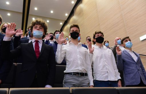 Czworo studentów w białych koszulach i marynarkach oraz maskach trzyma podniesione prawe dłonie i składa ślubowanie.