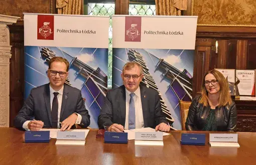 Dyrektor Jan Filocha, rektor prof. Krzysztof Jóźwik i kwestor PŁ Agnieszka Kobalczyk siedzą przy drewnianym stole. Przed nim umowy i pióra. W tle dwa roll upy uczelni.