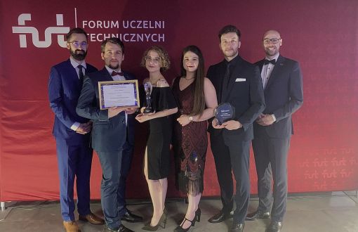 Elegancko ubrani studenci PŁ nagrodzeni na gali środowiskowej Forum Uczelni Technicznych stoją na tle bordowej ścianki.