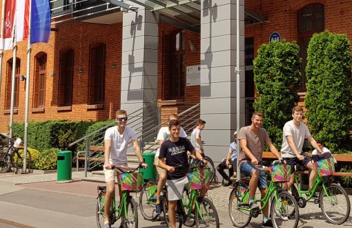 Studenci PŁ na rowerach przed ceglanym budynkiem IFE.
