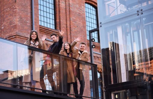 Czworo młodych ludzi stoi na tle nowoczesnej zabudowy.