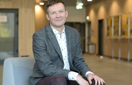 mężczyzna w średnim wieku uśmiecha się na zdjęciu, siedząc z dłońmi na kolanach opartymi