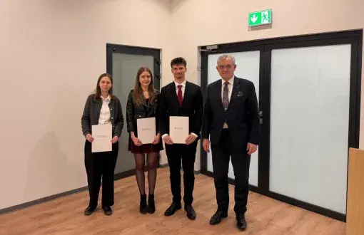 Troje młodych osób z dyplomami w rękach stoi w towarzystwie eleganko ubranego mężczyzny