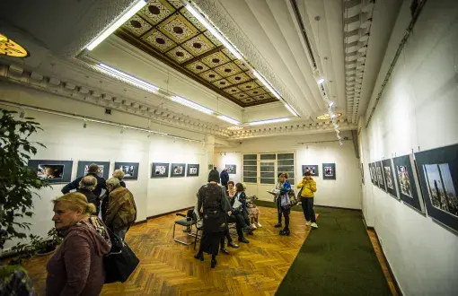 wnętrze zabytkowego budynku, zdobiony sufit, parkietowa podłoga, na ścianach obrazy, po środku kilka osób zwiedzających