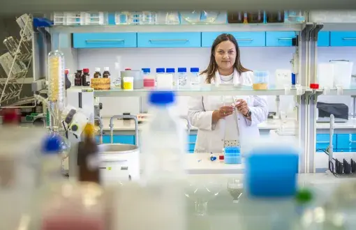 wnętrze laboratorium chemicznego, w głębi uśmiechnięta młoda badawczka w białym fartuchu