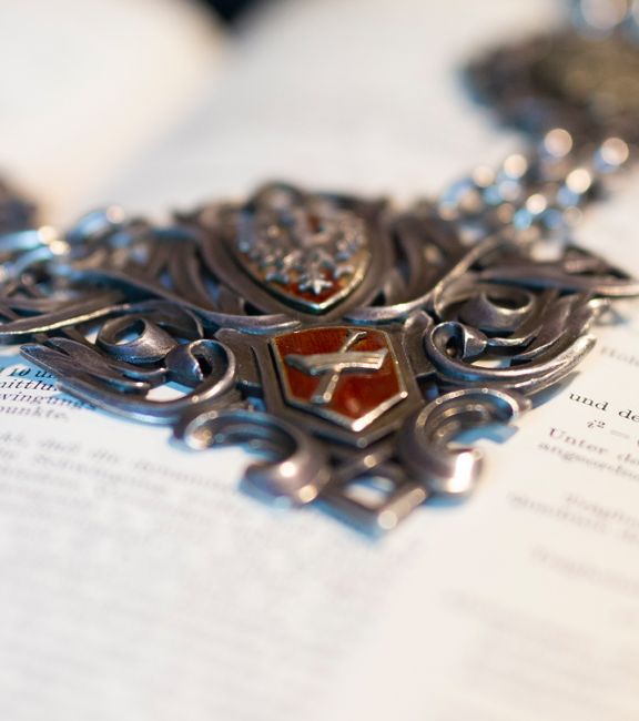 Fragment łańcucha rektorskiego na tle otwartej księgi.