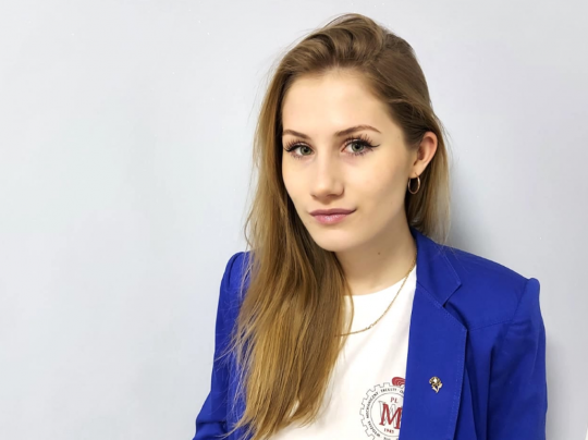 Portrait photo: Kateryna Bodko in blue jacket and light t-shirt on a grey wall.